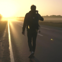 A lone traveler walking on an empty road at sunrise, soft golden light, slow-motion wind blowing clothes, cinematic camera movement, shallow depth of field, ultra-realistic, 4K, dramatic mood